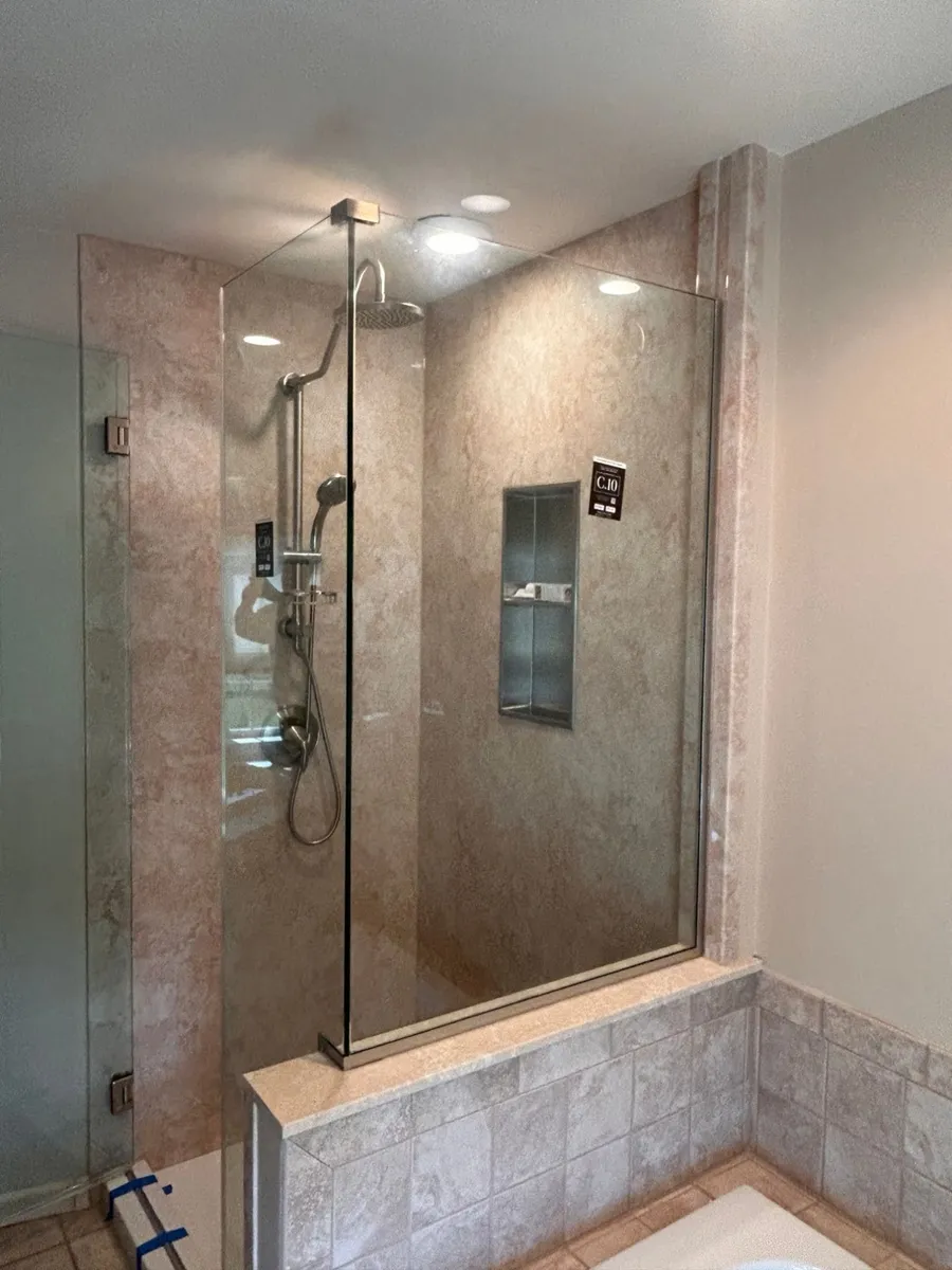 Corner view of the frameless glass enclosure on the tiled half wall
